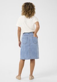 Džínová midi sukně ve světle modré barvě, s vysokým pasem, zadními kapsami a mírně áčkovým střihem, v kombinaci s volným bílým tričkem.