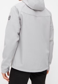 Hellgraue Softshelljacke mit Kapuze, glatter Textur und einem Logopatch am linken Ärmel. Reguläre Passform mit geradem Saum.