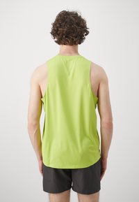 Světlezelené bezrukávové sportovní tričko z hladkého, prodyšného materiálu, s pohodlným střihem a zakřiveným spodním lemem, kombinované s černými šortkami.