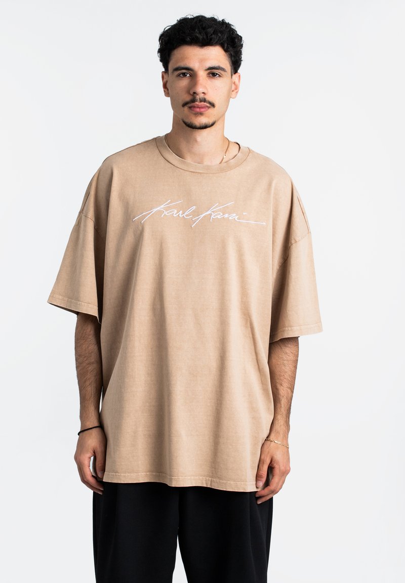 Per didelė beigi spalvos t-shirt, pagaminta iš minkštos medvilnės, su baltu, kursyvu parašytu logotipu ant priekinės pusės ir trumpomis rankovėmis, su atsipalaidavusiu siluetu.