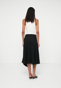 Melna svārku ar asimetrisku apakšmalu un zeltītiem kniedēm jostasvietā. Valkā ar baltu krūšturi un melniem augstpapēžu apaviem.