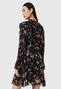 Vestido negro con flores, mangas con volantes y falda de capas, con la parte trasera recogida que incluye una pequeña abertura en forma de llave. Fabricado con tela ligera.