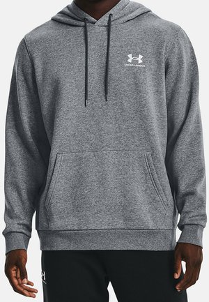Mężczyzna w szarej bluzie z kapturem Under Armour z przednią kieszenią i czarnymi troczkami na jednolitym tle.