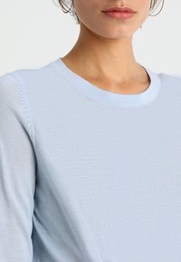 Jasnoniebieski sweter dzianinowy z okrągłym dekoltem i ribbową strukturą, z subtelnymi detalami wzdłuż szwu na ramieniu.