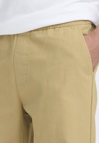 Pantaloni kaki con una texture liscia, dotati di tasche laterali, taglio dritto e cuciture visibili lungo le cuciture.