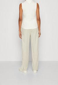 Hihaton, vaalean kermaisen värinen toppi, joka on yhdistetty löysiin, vaalean beigeihin housuihin. Sujuva pinta ja rento istuvuus, jossa on sivuväli aukoilla helmoissa.