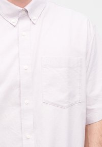 Ανοιχτό μοβ κοντομάνικο πουκάμισο με κουμπιά, μπροστινή τσέπη και εμφανή κουμπιά στη λωρίδα και το γιακά.