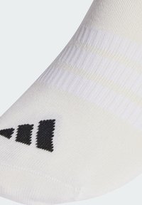 Calcetín atlético blanco con textura de canalé, que presenta tres rayas negras y un logo negro cerca de la puntera. Diseño ligero y ajustado.