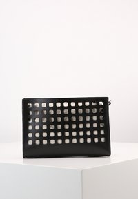 Černá kožená taška ve tvaru obalu s otevřeným mřížkovaným designem, obsahující čtvercové výřezy a zipové zapínání. Hladká textura s minimalistickým estetickým vzhledem.