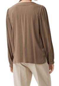 Blouse marron à manches longues avec une texture douce, des épaules plissées et un col. Dotée de poignets boutonnés et d'une coupe décontractée.