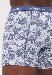 Weiße Boxershorts mit blauem Palmbaumdruck, ausgestattet mit einem blauen Bund mit "BJÖRN BORG"-Logo und flachen Nähten für zusätzlichen Komfort.