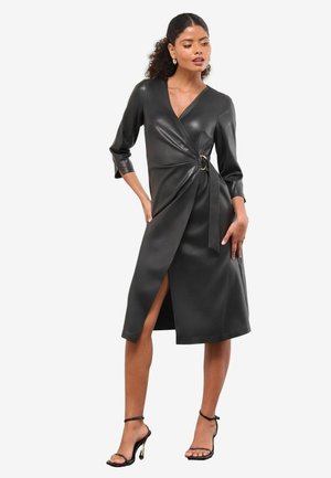 Melna mākslīgās ādas apmetņu kleita ar trim ceturtdaļām piedurknēm, sānu izgriezumu un sprādzi akcentā jostasvietā. Gluda, pieguļoša forma.