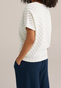 Biały dzianinowy top z wzorem w jodełkę, krótkimi rękawami i swobodnym krojem. W zestawie z ciemnoniebieskimi szerokimi spodniami.