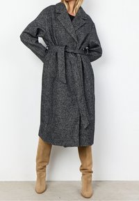 Szary wełniany płaszcz w wzór jodełki z paskiem w talii, dużymi klapami, dwoma guzikami i bocznymi kieszeniami. Zestawiony z beżowymi botkami do kolan.