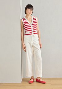 Top sin mangas a rayas rojas y blancas con detalle de botones, combinado con pantalones anchos blancos y zapatos planos rojos. Texturas suaves, ajuste casual.
