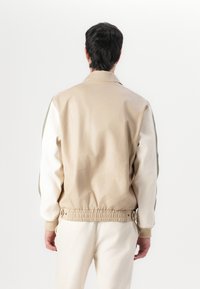 Tan- und weiße Bomberjacke mit elastischem Taillengummi und Bündchen, ausgestattet mit einer glatten Textur und kontrastierenden Schulterpanelen in Olivgrün.