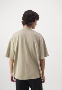 Košile s krátkým rukávem v oversize stylu v khaki barvě, s hladkým povrchem a uvolněným střihem. Disponuje kulatým límcem a volně sedí kolem těla.