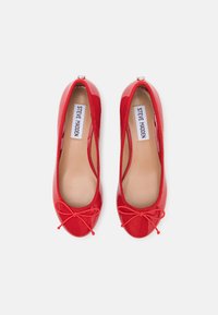 Red patent leather ballet flats with a rounded toe, elasticized edge, and a bow detail at the front. Inside has a beige lining.