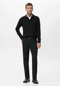 Suéter negro de punto con cuello, combinado con pantalones negros y zapatos negros brillantes. El atuendo tiene un corte ajustado y una textura suave.