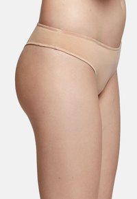 Ropa interior de algodón beige con una textura suave, diseño de cintura baja y cobertura mínima. La cinturilla es elástica y coincide con el color de la tela.