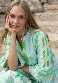 Vestido ligero con un patrón geométrico en turquesa y verde, con mangas abullonadas y un escote redondo, contra un fondo natural.