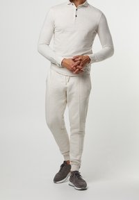 Vaaleanbeige pitkähihaista poolopaitaa, jossa on kaulus ja kolme nappia, parina sopivat kapenevat collegehousut, joissa on sivusauman yksityiskohtia ja kiristysnauha.