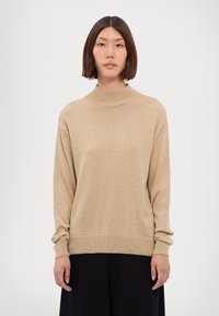 Maglione a collo alto beige in un morbido tessuto a maglia, con maniche lunghe e una vestibilità rilassata; i polsini e l'orlo a coste aggiungono un tocco di dettaglio sofisticato.