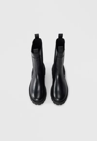 Black leather ankle boots with a glossy finish, featuring elastic side panels, pull tabs, and rugged rubber soles for traction.