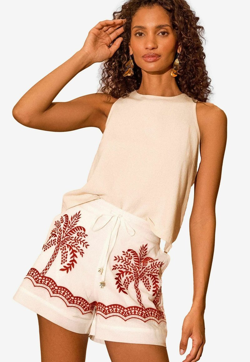 Beige bez piedurknēm tops, kas apvienots ar baltām šortiem, ar sarkanu palmu koka izšuvumu un viļņveida rakstu apmalē. Ar aukliņu regulējamā jostas daļa.