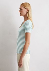 Camiseta de cuello en v a rayas en azul claro y blanco, de mangas cortas, diseño ajustado, hecha de tela suave y con un pequeño logo en el dobladillo.