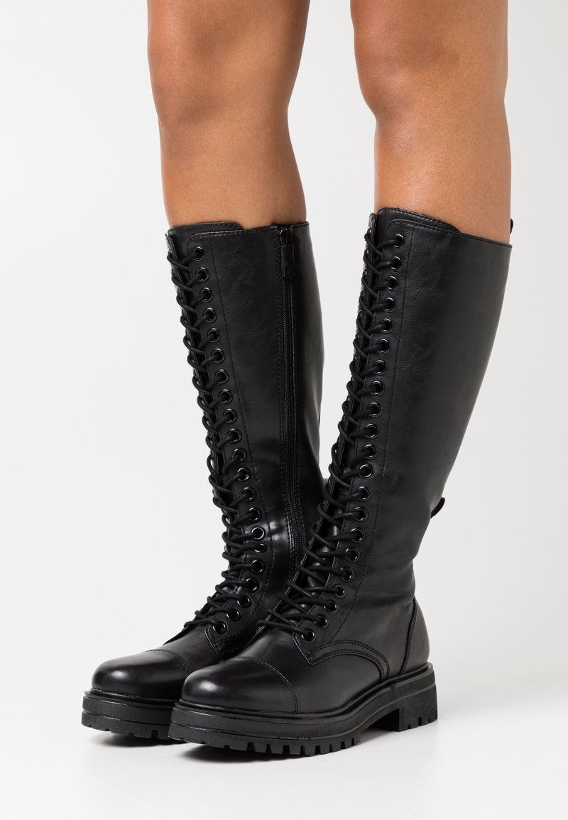 Mustat polvipituiset saappaat, jotka on valmistettu sileästä nahasta. Niissä on edessä nauhoitus, kestävä kumipohja ja sivu-zip, joka helpottaa pukemista.