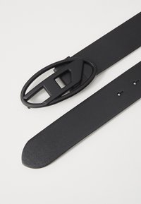 Cinturón de cuero negro que presenta una hebilla redondeada con un detalle de corte geométrico. La correa es lisa y tiene cinco agujeros de ajuste.