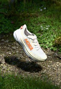La chaussure de course Hoka présente un dessus en mesh jaune clair avec des accents orange, une semelle intermédiaire rembourrée et une semelle extérieure noire texturée pour une meilleure traction.
