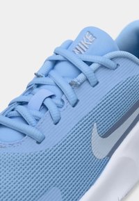 Jasnoniebieski but sportowy Nike z teksturowaną tkaniną, siateczkowymi detalami i płaskimi sznurówkami. Na boku widoczny charakterystyczny srebrny znak Nike swoosh.