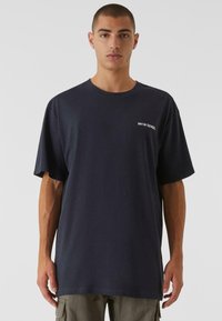 Námořnická modrá oversized tričko z jemné bavlny, s kulatým výstřihem a malým bílým potiskem loga na hrudi. Pohodlný, volný střih.
