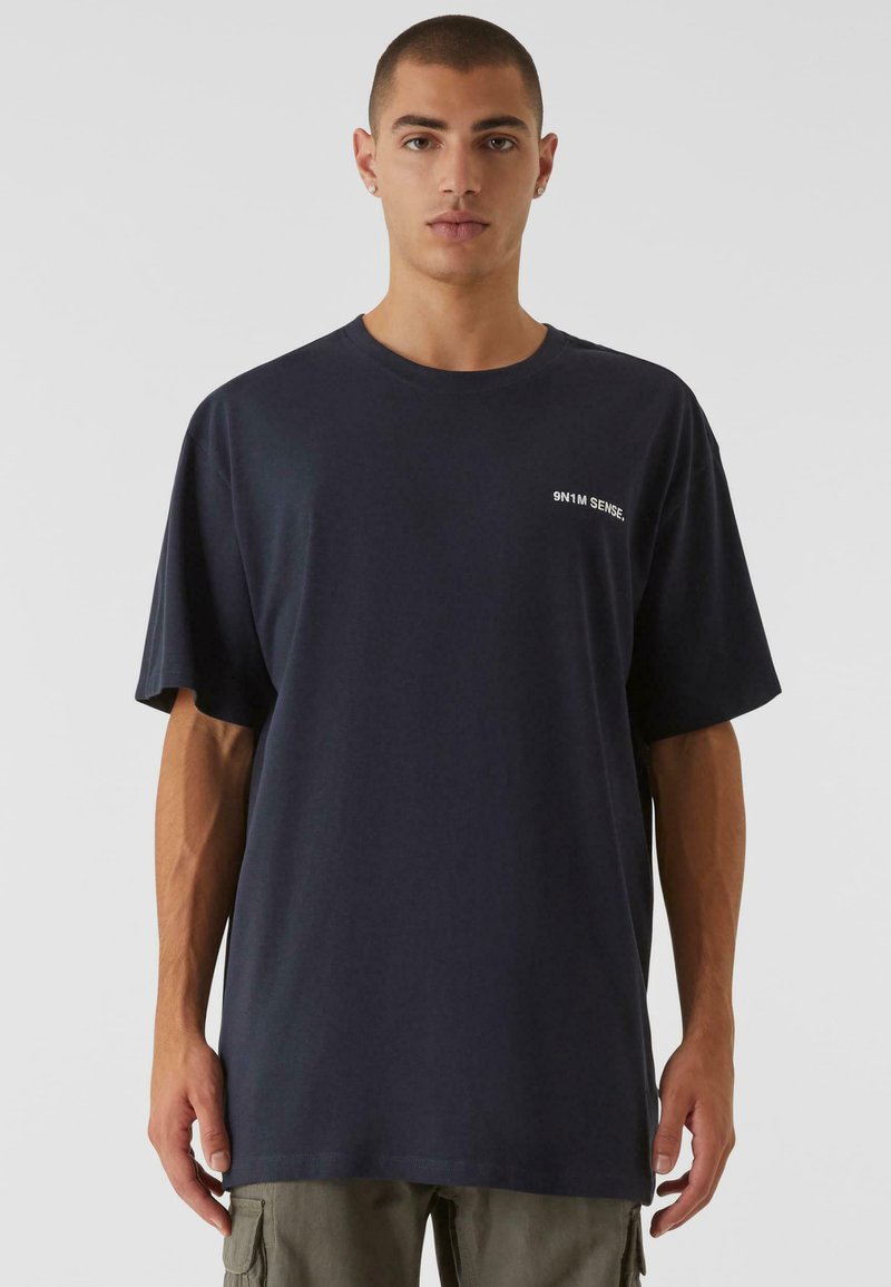 Námořnická modrá oversized tričko z jemné bavlny, s kulatým výstřihem a malým bílým potiskem loga na hrudi. Pohodlný, volný střih.