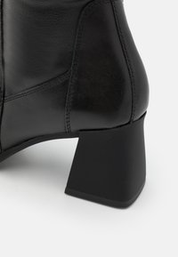 Bota de cuero negra hasta el tobillo con tacón ancho. Presenta una textura suave, costuras reforzadas y un diseño de puntera redonda.