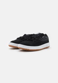 Black suede sneakers with mesh accents, white midsole, and brown rubber outsole. Laced design. Low-top profile with subtle branding.