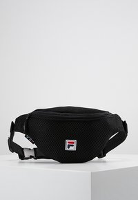 Borsello in tessuto a rete nera con zip frontale e patch logo Fila, cintura regolabile e chiusura a fibbia su una piattaforma bianca.