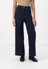Jeans de ganga escura de cintura alta com corte largo, apresentando dois bolsos frontais e um fecho de botão visível. Textura suave.