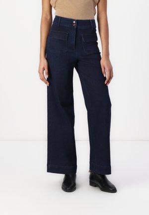 Jeans en denim bleu foncé taille haute avec une coupe évasée, dotés de deux poches avant et d'une fermeture avec bouton visible. Texture lisse.