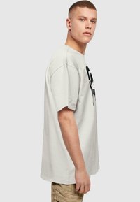 Tricou oversized de culoare gri deschis, confecționat din bumbac, cu un design grafic negru pe față, mâneci scurte și guler rotund.
