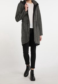 Šedý kabát do délky ke kolenům s kapucí, zipovým uzávěrem a stahovacími šňůrkami. Obsahuje kovové akcenty a texturovanou tkaninu. Nosený na černých kalhotách a botách.