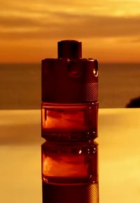 Amberfärgad glasparfymflaska med en texturerad silverkapsyl, med cylindrisk form och en slät, reflekterande yta.