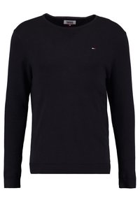 Pull en tricot noir avec des manches longues, col en V, poignets et ourlet côtelés. Présente un petit logo avec des accents rouge, blanc et bleu sur la poitrine.