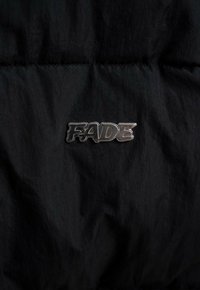 Czarna kurtka puchowa z błyszczącą srebrną naszywką z logo "FADE" na przodzie. Materiał wydaje się gładki z delikatnym połyskiem.