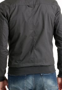 Czarna bomberka o gładkiej fakturze, z prążkowanym dołem i mankietami. Posiada plisę z tyłu i brak widocznych metalowych elementów. Noszona z niebieskimi dżinsami.