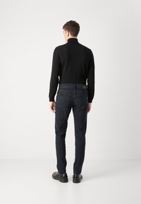 Tumedat teksad, mis on slim fit stiilis, koos musta pika varrukaga toppiga. Teksadel on klassikaline viie taskuga disain ja silt seljal.