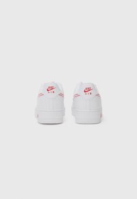 Hvide lædersneakers med røde accenter. Funktioner inkluderer en glat overflade, afrundet form og synlig Nike-logo på hælen og siden.