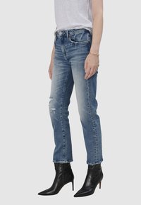 Jasnoniebieskie dżinsy o slim fit, z przetarciami i wyblakłym wykończeniem, w zestawieniu z czarnymi, spiczastymi botkami za kostkę.